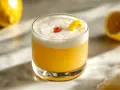Amaretto sour przepis: puszysty koktajl z pianką, wisienką i skórką cytrynową. Idealny na letnie wieczory.