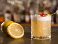 Orzeźwiający drink z amaretto, ozdobiony wisienką i plasterkiem cytryny, obok świeżych cytryn na barze.