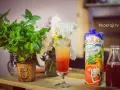 Kolorowy drink z lodem i słomkami, obok sok grejpfrutowy Hortex i butelka z ciemnym płynem.