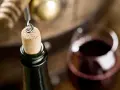 Korek wyciągany z butelki wina, kieliszek czerwonego wina i beczka. Czy wino ma datę ważności? To pytanie zadaje sobie wielu miłośników tego trunku.