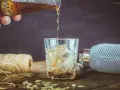 Nalewanie drinka z amaretto i wódką do szklanki z lodem. Na stole płatki migdałów i sznurek.