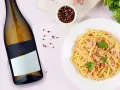 Idealne jakie wino do carbonary? Obok talerza z pysznym makaronem i butelki białego wina, pieprz i natka pietruszki.
