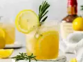 Szklanka z drinkiem z cytryną i rozmarynem, w tle butelka alkoholu i cytryny.