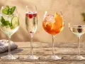 Cztery drinki na drewnianym stole: mojito, prosecco z malinami, Aperol Spritz i kieliszek prosecco z jeżyną. Idealne inspiracje, jak pić prosecco i inne orzeźwiające napoje.