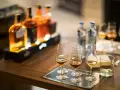 Degustacja whisky, czy to bimber? Butelki i kieliszki z bursztynowym trunkiem na drewnianym stole.
