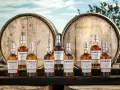 Butelki whisky BenRiach stoją przed beczkami, sugerując skąd pochodzi whisky.