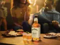 Jack Daniel's Honey z czym pić? Idealnie smakuje solo, z lodem lub jako dodatek do drinków. Na stole ser, winogrona i przekąski.