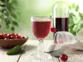 Wytrawne wino z owocami wiśni, podane w ozdobnym kieliszku, z miseczką pełną świeżych wiśni w tle.