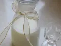 Biały płyn w karafce ozdobionej wstążką, obok pusty kieliszek. Idealne do przygotowania drinków, np. jak zrobic Malibu.