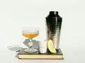 Elegancki kieliszek z bursztynowym trunkiem, shaker, plasterek cytryny i biały kubeczek z napisem "MIXING GLASS" – wszystko to sugeruje, z czym pić whisky, by stworzyć wyrafinowany koktajl.
