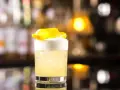 Orzeźwiający drink z whisky i miodem, ozdobiony skórką cytryny, na tle rozmytego baru.