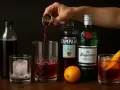 Jaki wermut do negroni? Na zdjęciu widać składniki: gin, Campari, pomarańczę i butelkę z ciemnym płynem.