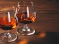 Dwa kieliszki z bursztynowym płynem, być może amerykańska whisky z kukurydzy, stoją na drewnianym stole.