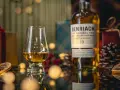 Szklanka z bursztynowym single malt whisky Benriach 10, obok butelki i świątecznych dekoracji.