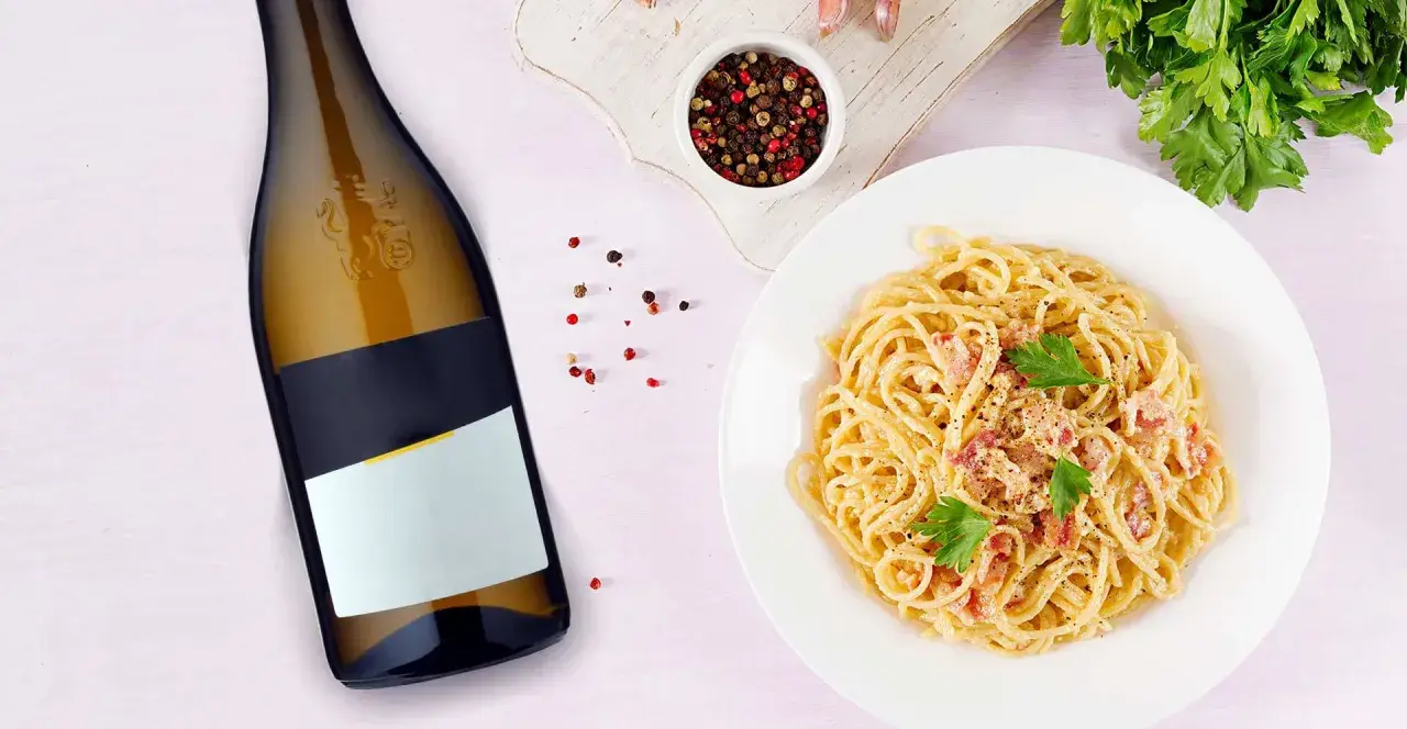 Idealne jakie wino do carbonary? Obok talerza z pysznym makaronem i butelki białego wina, pieprz i natka pietruszki.