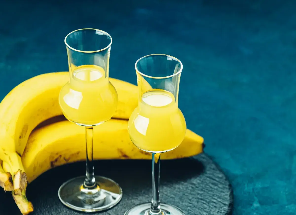 Dwa kieliszki z żółtym likierem bananowym, obok pęk bananów. Idealny na domowy likier bananowy przepis.