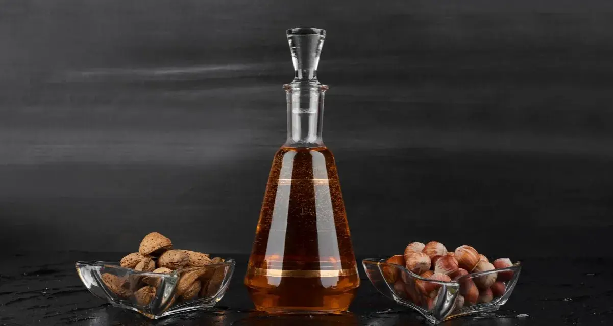 Amaretto co to? Bursztynowy likier w karafce, obok miseczki z migdałami i orzechami laskowymi.
