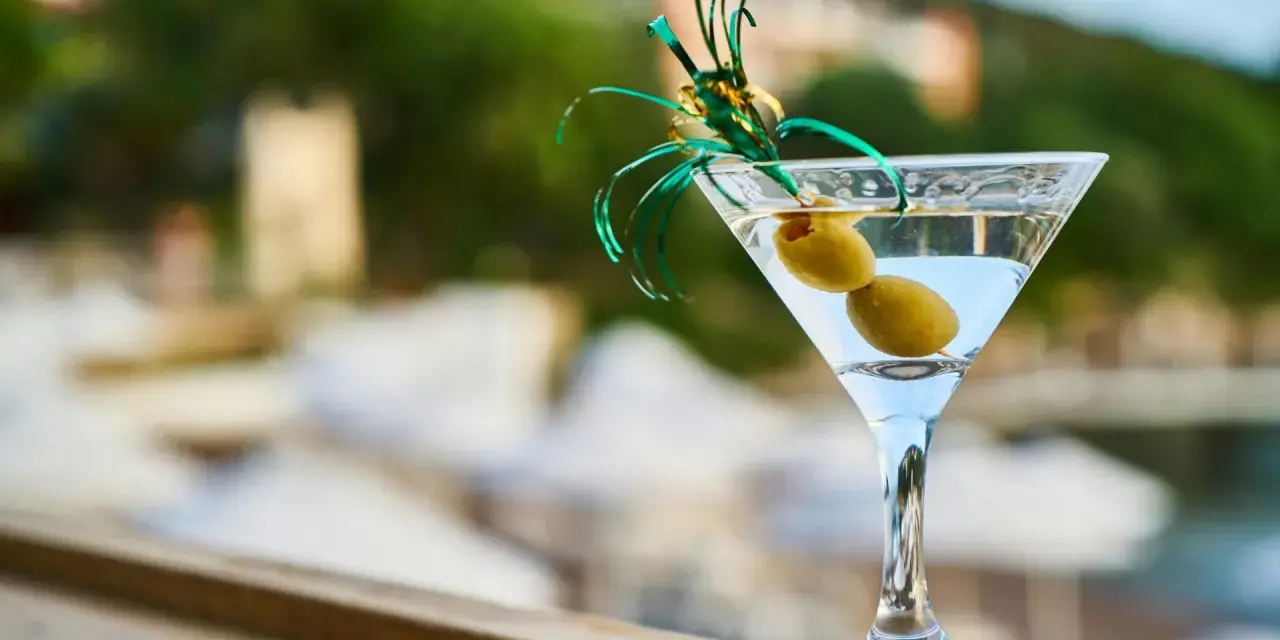 Idealny drink na wakacje: schłodzone martini z dwiema oliwkami, ozdobione zieloną wstążką. Idealne co do martini.
