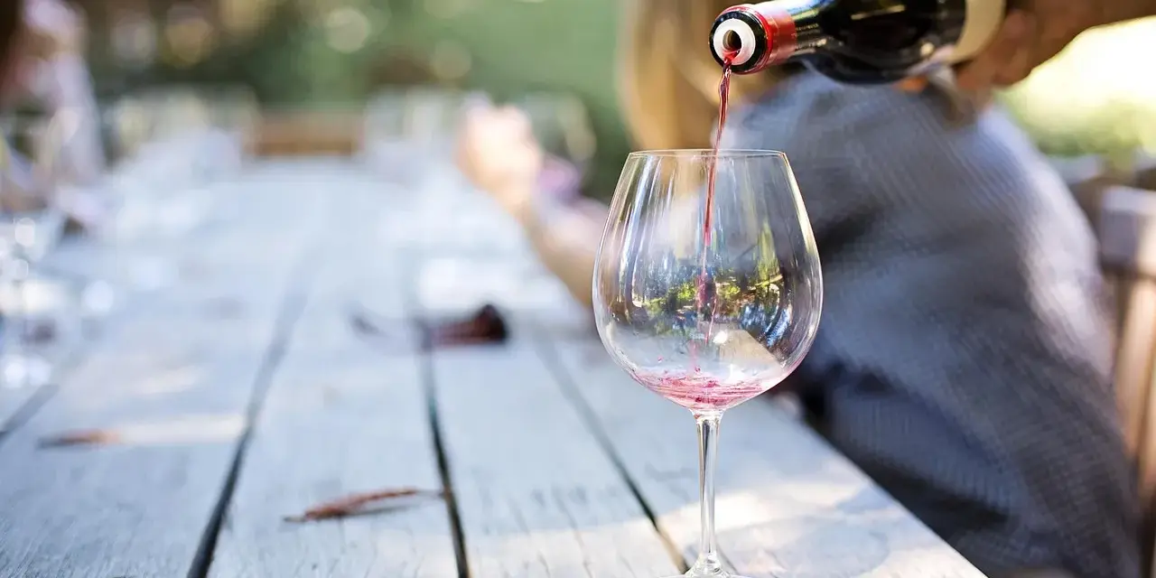 Czerwone wino nalewane do kieliszka na drewnianym stole. Idealny moment, by dowiedzieć się, jak degustować wino.