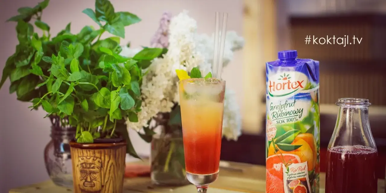 Kolorowy drink z lodem i słomkami, obok sok grejpfrutowy Hortex i butelka z ciemnym płynem.