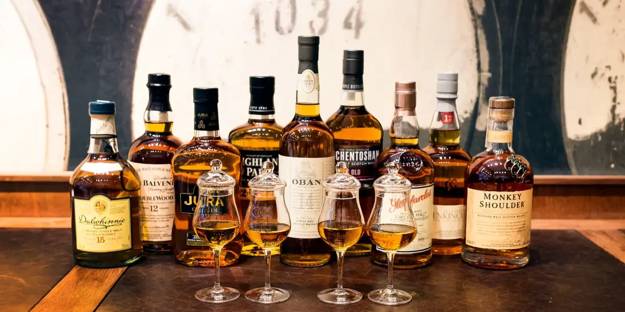 Wybór między single malt czy blended: rząd butelek szkockiej whisky, cztery kieliszki z bursztynowym płynem.