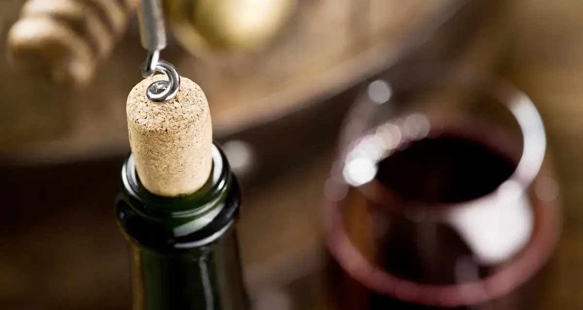 Korek wyciągany z butelki wina, kieliszek czerwonego wina i beczka. Czy wino ma datę ważności? To pytanie zadaje sobie wielu miłośników tego trunku.