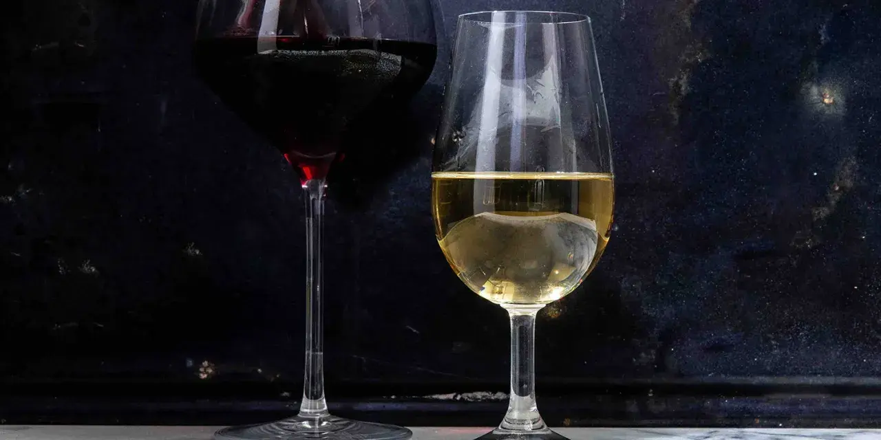 Dwa kieliszki z winem: czerwonym i białym. Białe wino, w tym wino extra dry, lśni w świetle.