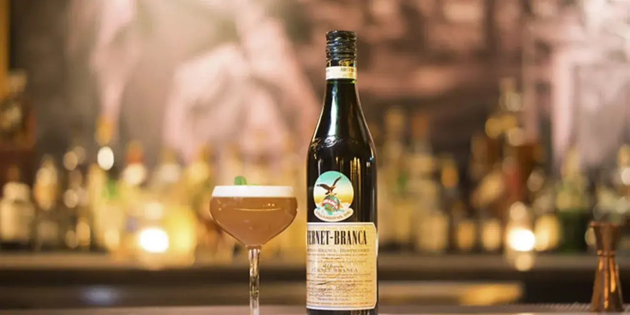 Fernet Stock z czym pić? Oto propozycja drinka z butelką Fernet-Branca i kieliszkiem koktajlu na barze.