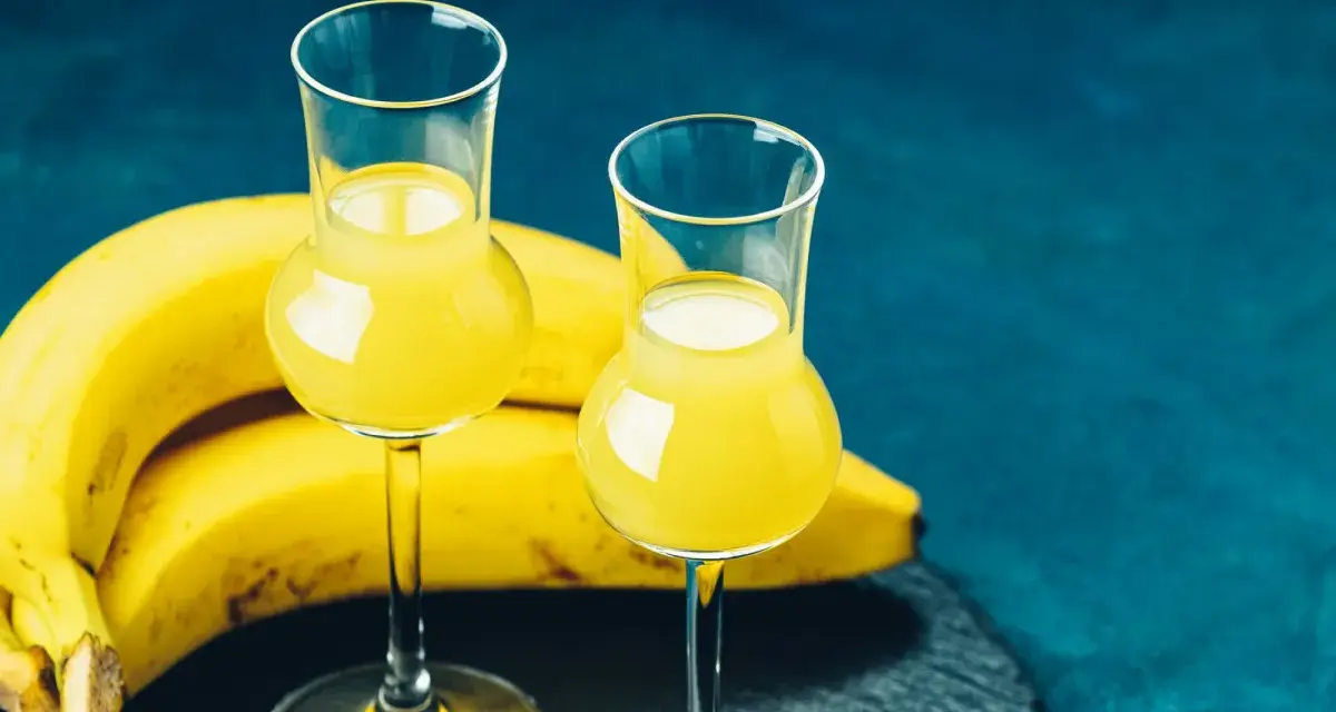 Dwa kieliszki z żółtym likierem bananowym, obok pęk bananów. Idealny na domowy likier bananowy przepis.