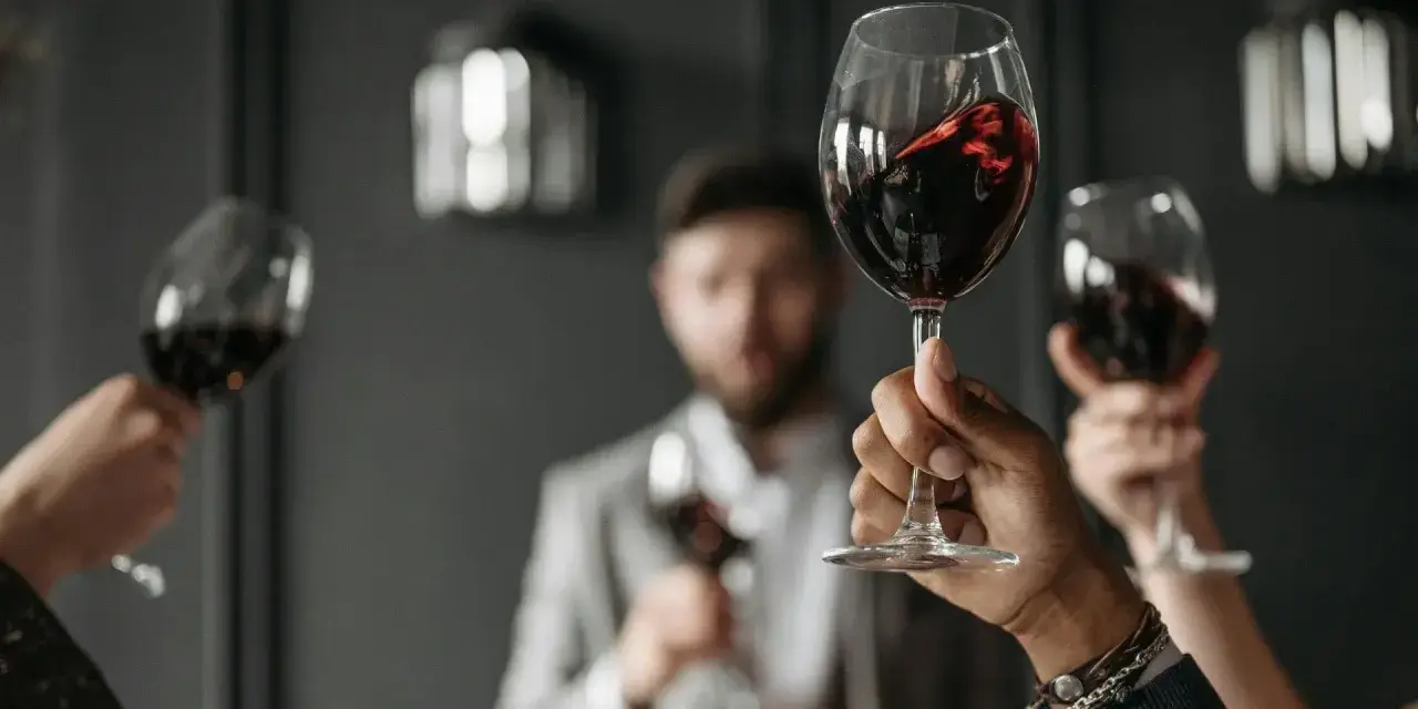 Wzniesione kieliszki z czerwonym winem, w tle mężczyzna w garniturze. Ciesz się chwilą z dobrym winem w kieliszku.