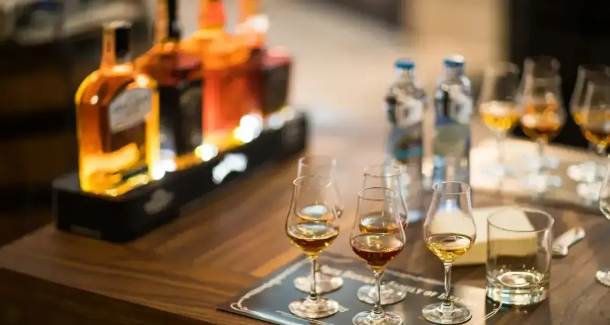 Degustacja whisky, czy to bimber? Butelki i kieliszki z bursztynowym trunkiem na drewnianym stole.