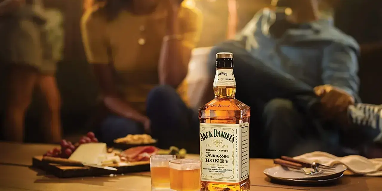 Jack Daniel's Honey z czym pić? Idealnie smakuje solo, z lodem lub jako dodatek do drinków. Na stole ser, winogrona i przekąski.