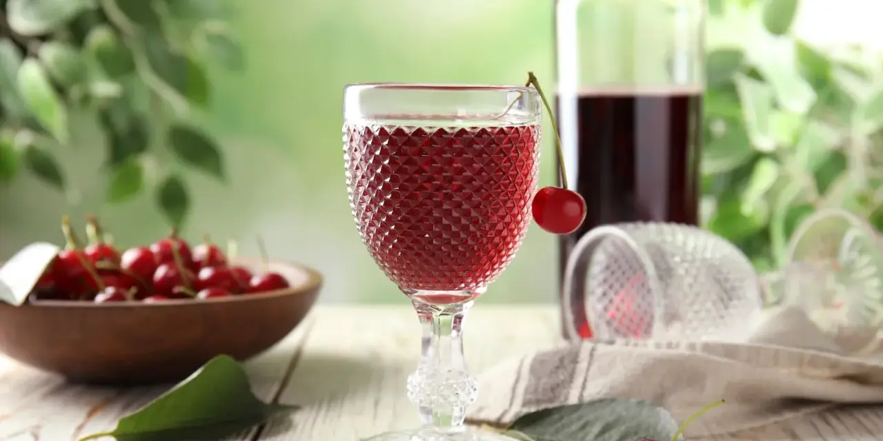 Wytrawne wino z owocami wiśni, podane w ozdobnym kieliszku, z miseczką pełną świeżych wiśni w tle.