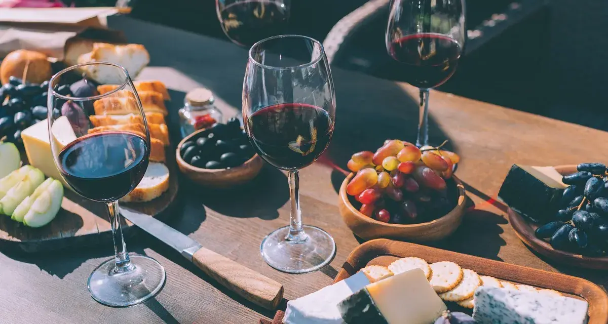 Degustacja merlot: jakie to wino? Kieliszki pełne czerwonego wina, deska serów, winogrona, oliwki i pieczywo tworzą idealną kompozycję.