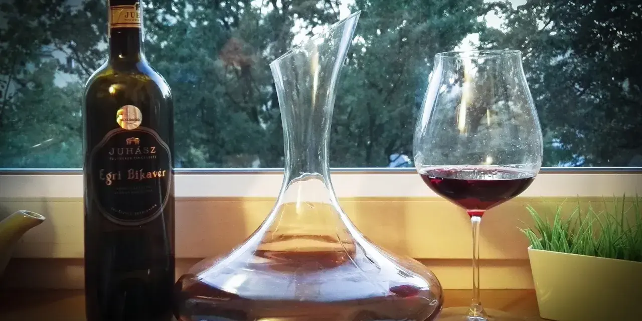 Butelka wina Egri Bikavér, karafka i kieliszek z czerwonym winem. Czas na degustację wina bycza krew.