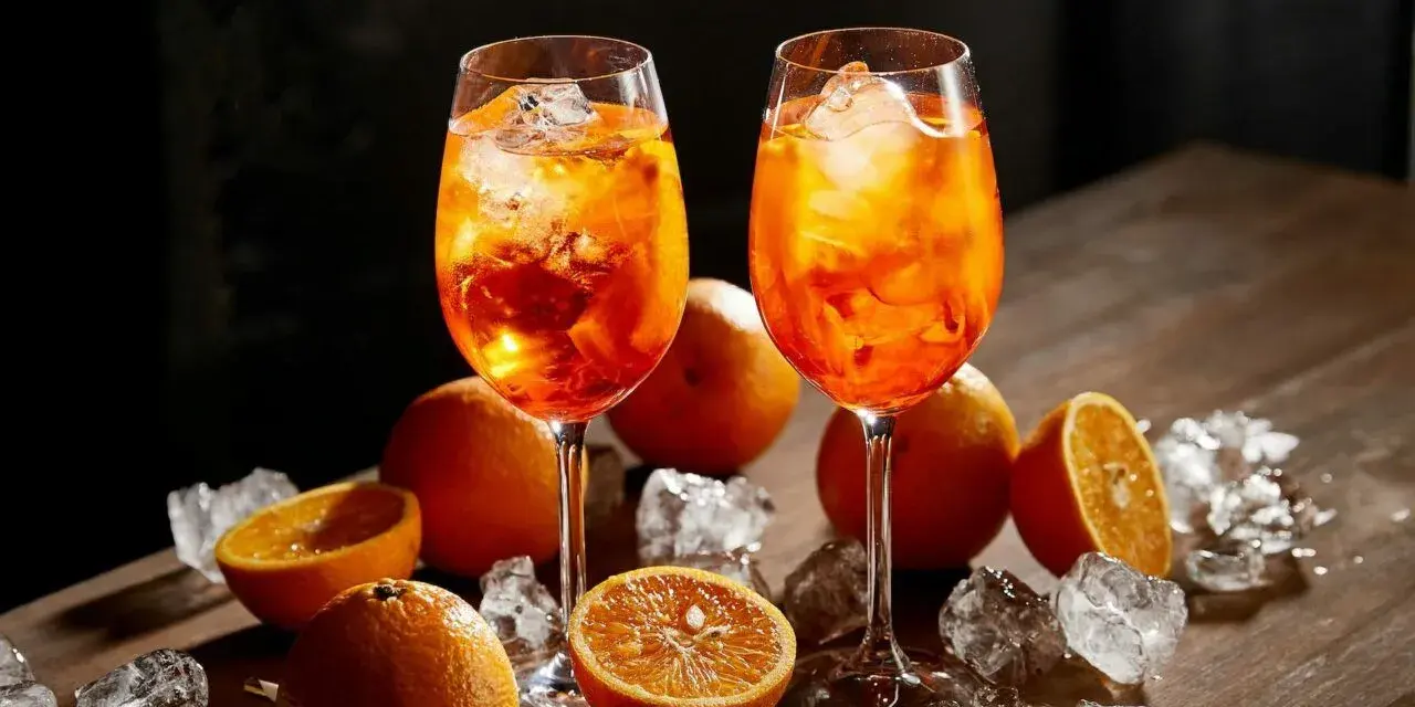 Dwa kieliszki orzeźwiającego aperol z colą, ozdobione pomarańczami i lodem, kuszą letnim smakiem.