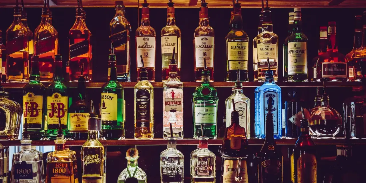 Różnorodne podstawowe alkohole do drinków: whisky, gin, tequila, likiery, stoją na półkach baru, gotowe do przygotowania koktajli.