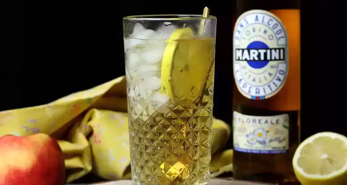 Orzeźwiający drink z Martini i lodem, ozdobiony plasterkiem cytryny. Obok jabłko i butelka Martini.