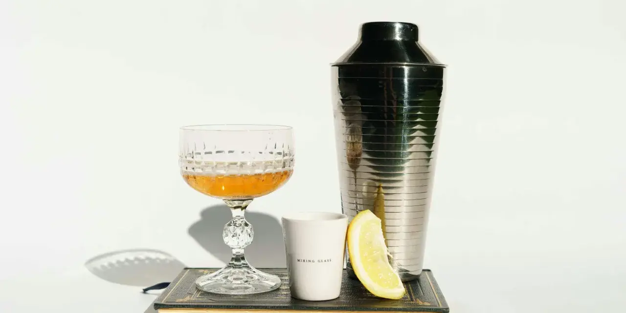 Elegancki kieliszek z bursztynowym trunkiem, shaker, plasterek cytryny i biały kubeczek z napisem "MIXING GLASS" – wszystko to sugeruje, z czym pić whisky, by stworzyć wyrafinowany koktajl.