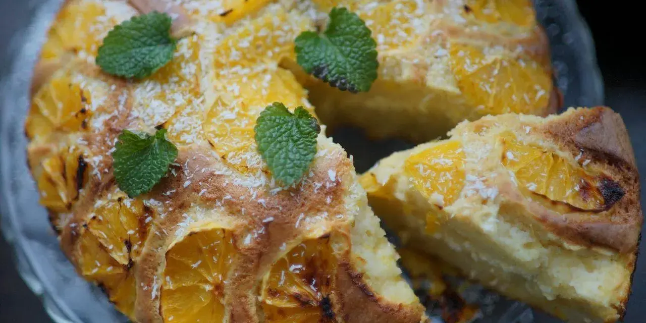 Ciasto z pomarańczami i wiórkami kokosowymi, ozdobione listkami mięty. Wyczuwalny aromat świeżego **zestu z cytryny** w cieście.