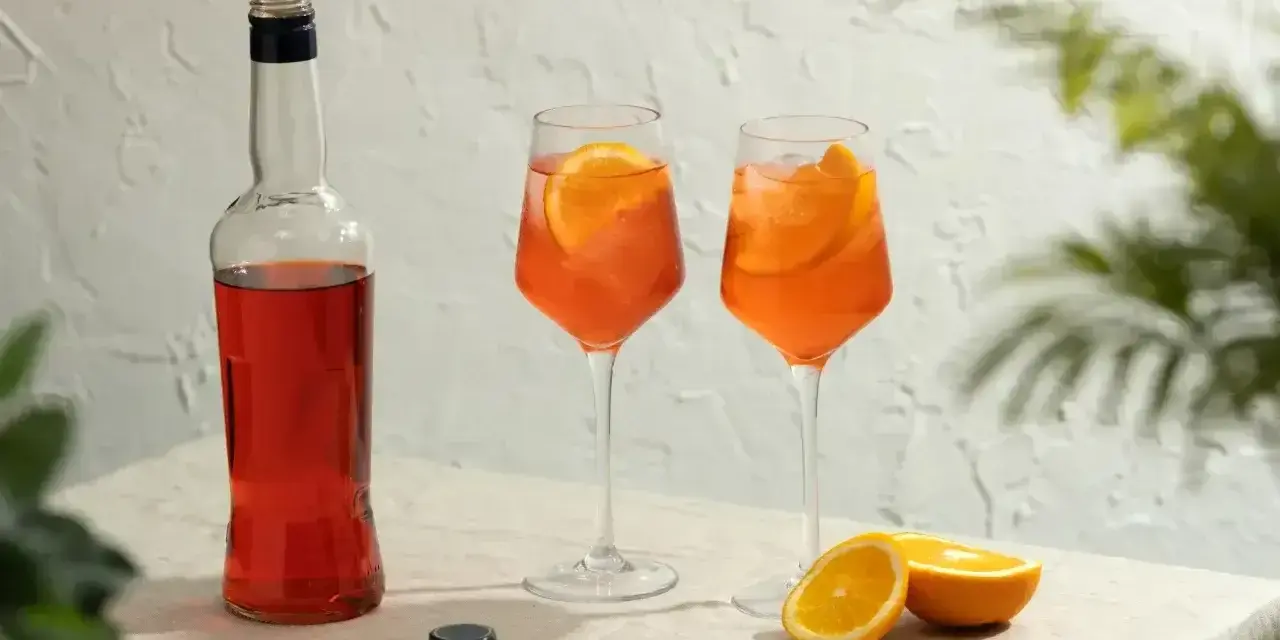 Dwa orzeźwiające drinki Aperol z plastrami pomarańczy i butelka Aperolu. Idealne na letnie popołudnie.