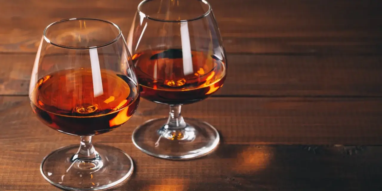 Dwa kieliszki z bursztynowym płynem, być może amerykańska whisky z kukurydzy, stoją na drewnianym stole.