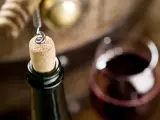 Korek wyciągany z butelki wina, kieliszek czerwonego wina i beczka. Czy wino ma datę ważności? To pytanie zadaje sobie wielu miłośników tego trunku.