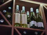 Butelki białego wina w drewnianym regale. Zastanawiasz się, ile może stać otwarte wino? Te butelki czekają na degustację.