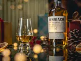 Szklanka z bursztynowym single malt whisky Benriach 10, obok butelki i świątecznych dekoracji.