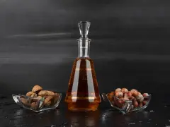 Amaretto co to? Bursztynowy likier w karafce, obok miseczki z migdałami i orzechami laskowymi.