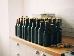 Rząd ciemnych butelek piwa z żółtymi kapslami, gotowych do degustacji. To początek drogi, jak zrobić piwo w domu.