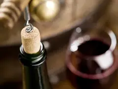Korek wyciągany z butelki wina, kieliszek czerwonego wina i beczka. Czy wino ma datę ważności? To pytanie zadaje sobie wielu miłośników tego trunku.