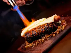 Czarny hot dog z serem i sezamem, podpalany palnikiem. To właśnie flambirowanie co to za technika!