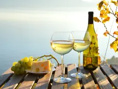 Dwa kieliszki białego wina wytrawnego, butelka, winogrona i ser na drewnianym stole. Zastanawiasz się, ile kalorii ma białe wino wytrawne?